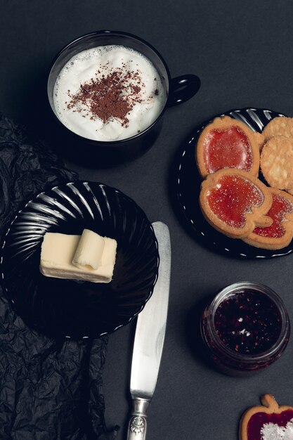 Taza de café, capuchino con galletas de chocolate y galletas en mesa negro. Tarde de descanso. Desayuno. Vista superior.