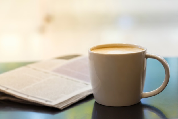 Taza de café capuchino en la mesa de madera con periódico