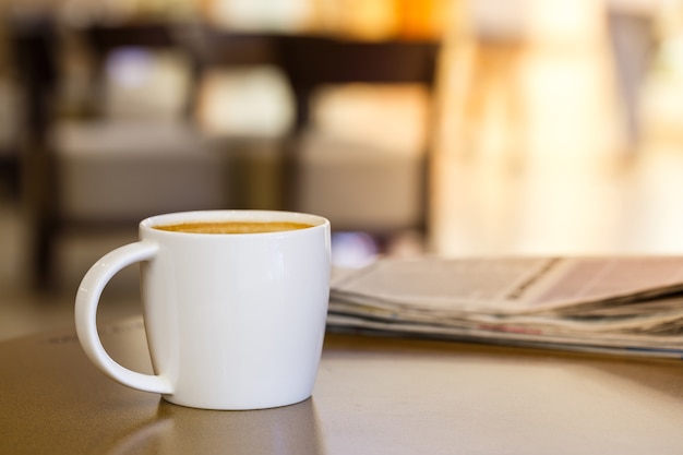 Taza de café capuchino en la mesa de madera con periódico