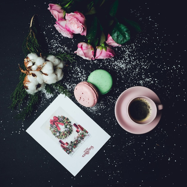 La taza de café se coloca en la mesa negra con los macarrones y las rosas