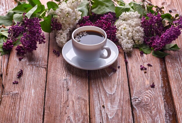 Taza de café y coloridas flores lilas en mesa de madera de jardín