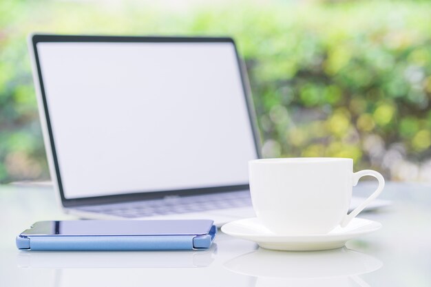 Taza de café y computadora portátil en la oficina con teléfono inteligente