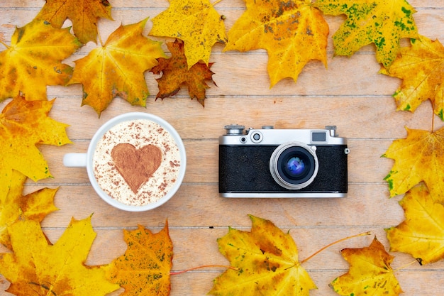 Foto taza de café con un corazón de canela y cámara sobre la mesa, hojas de arce alrededor