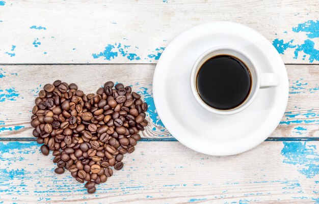 Taza con café y corazón de granos de café sobre fondo de madera.