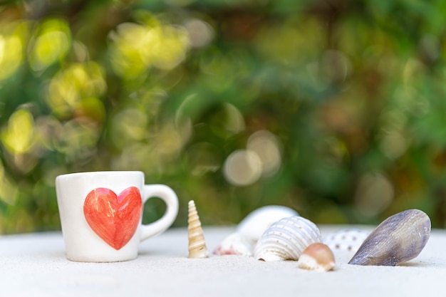 Foto taza de café con corazón rojo impreso en arena contra la naturaleza de fondo bokeh.