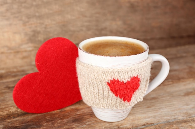 Taza de café con corazones de fieltro rojo sobre fondo de madera, cerrar