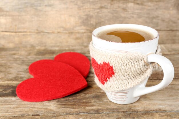 Taza de café con corazones de fieltro rojo sobre fondo de madera, cerrar