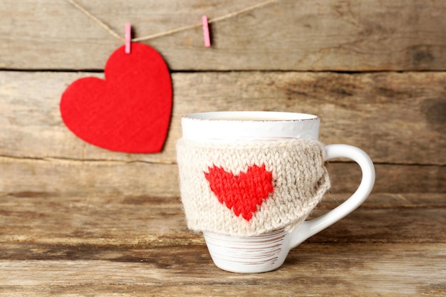 Taza de café con corazones de fieltro rojo sobre fondo de madera, cerrar