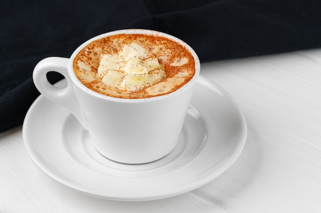 Taza de café con crema batida en la mesa blanca de cerca