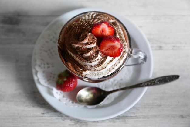 Taza de café con crema y fresas frescas sobre fondo de madera de color