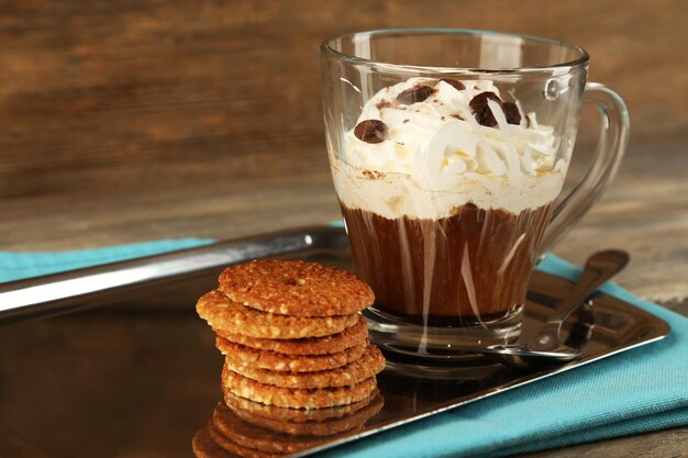 Taza de café con crema y galletas en bandeja de metal sobre fondo de madera