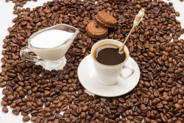 Taza de café, crema y galletas entre granos de café tostados. Vista superior