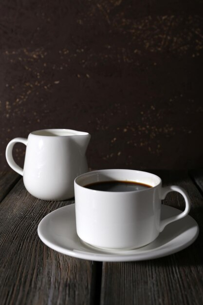 Foto taza de café y crema en jarra de leche sobre mesa de madera sobre fondo oscuro