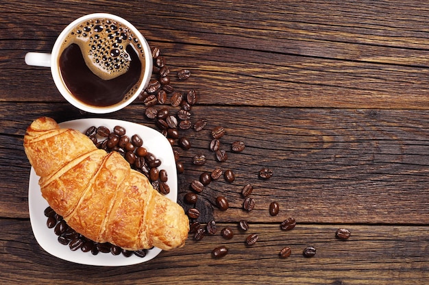 Taza de café con croissant para desayunar en una mesa de madera oscura, vista superior