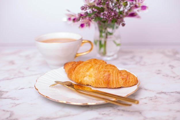 Taza de café y croissant dulce en mesa blanca decorada con un hermoso ramo de flores