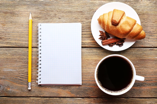 Taza de café con croissant recién hecho y hoja de papel en blanco en la vista superior de la mesa de madera