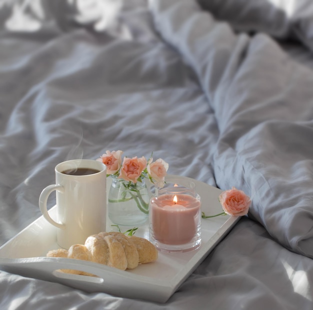 Taza de café con croissant y rosas rosas en la cama en el dormitorio