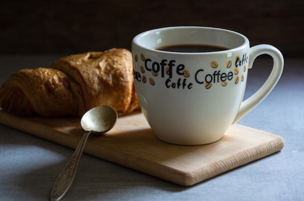 Taza de café y croissant en una tabla de madera.