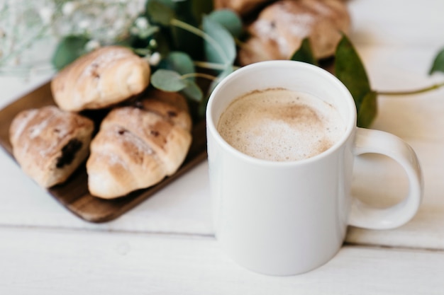 Foto taza de café con croissants y flores borrosas