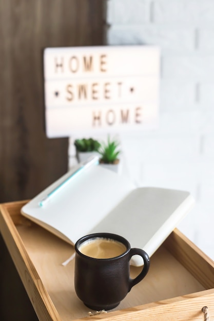 Una taza de café y un cuaderno abierto en una bandeja de madera