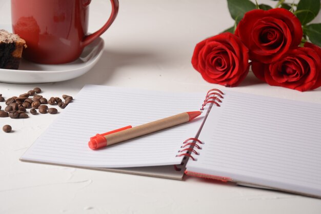 Taza de café, cuaderno, bolígrafo y flores color de rosa Pausa para el café de la mañana