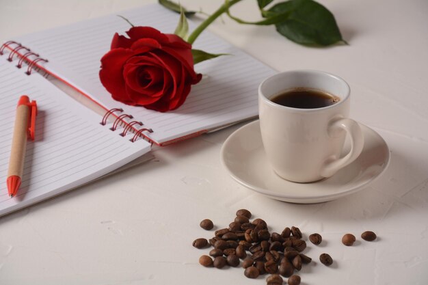 Taza de café, cuaderno, bolígrafo y flores color de rosa Pausa para el café de la mañana