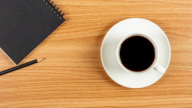 Taza de café y un cuaderno en el escritorio de oficina de madera. - espacio en blanco para texto publicitario.