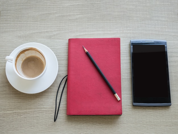 Una taza de café con un cuaderno y una tableta en la mesa
