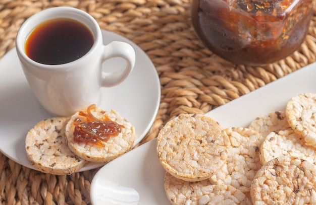 Una taza de café debajo de la mesa de paja rodeada por un cuenco lleno de galletas de arroz y una olla de gelatina