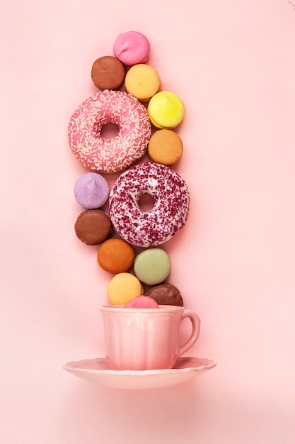 Taza de café, deliciosas rosquillas rosas con espolvorear y coloridos macarons brillantes