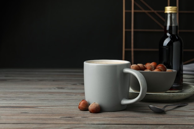 Taza de café delicioso con jarabe de avellana en un espacio de mesa de madera para el texto