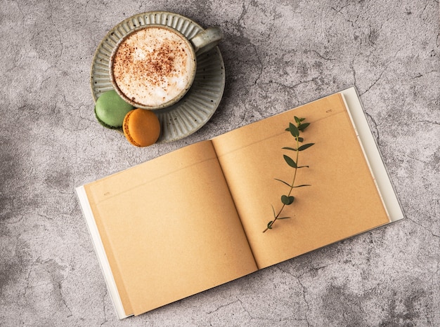 Taza de café para el desayuno, macarrones, cuaderno vacío sobre una mesa de hormigón gris