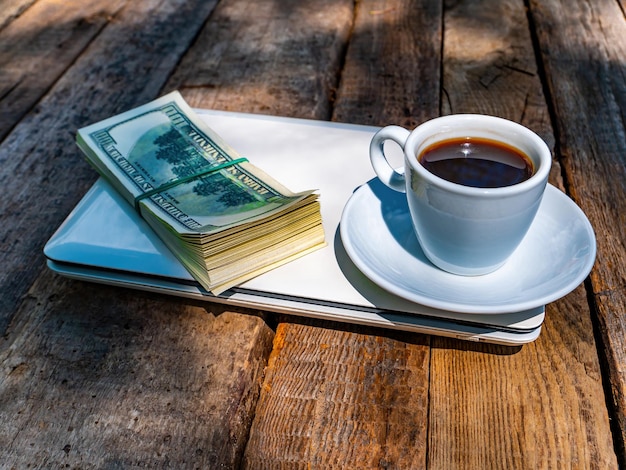 Una taza de café y dinero con una computadora portátil se encuentran en una mesa de madera