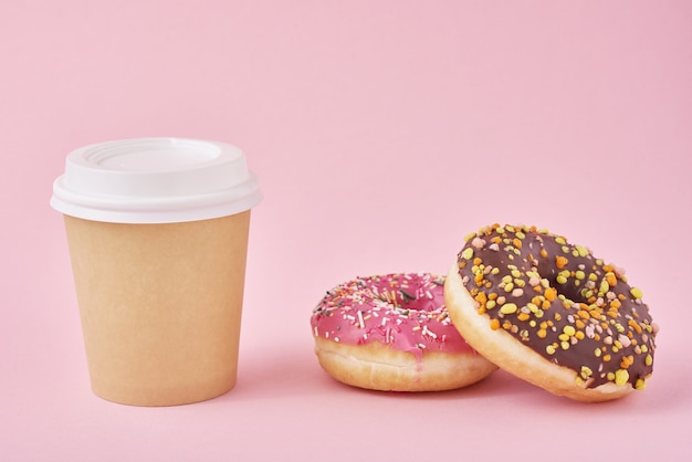 Taza de café y donas en superficie rosa