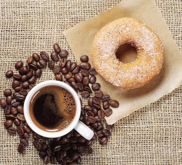 Taza de café y donut con azúcar sobre un fondo de arpillera Vista superior