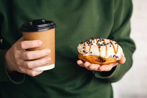 Una taza de café y un donut en manos masculinas de cerca