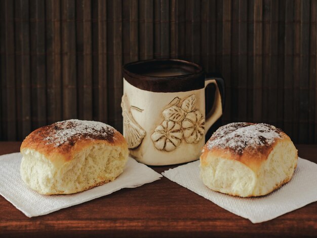 Una taza de café y dos bollos sobre un fondo de madera oscura.