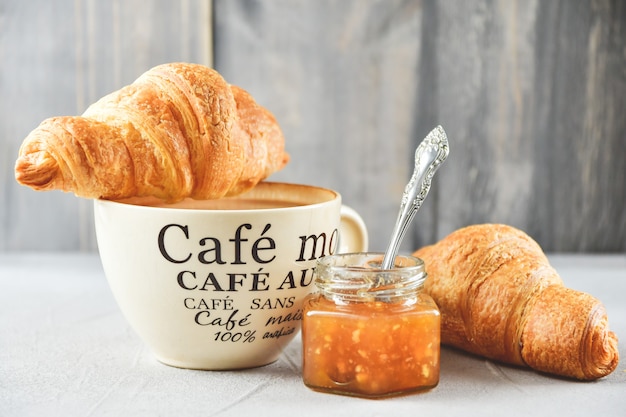 taza de café, dos croissants y mermelada de manzana en un frasco de vidrio