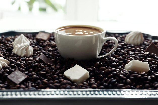 Taza de café con dulces y granos de café en una bandeja