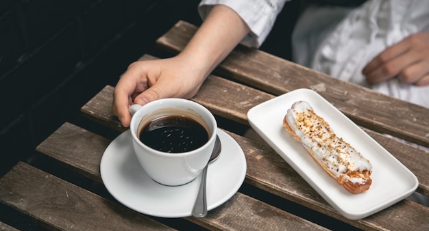 Taza de café y eclair en un primer plano de la mesa de madera