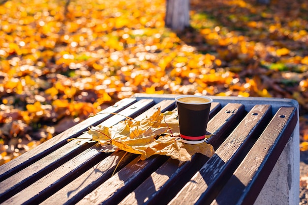 Una taza de café se encuentra en un banco con hojas de otoño.