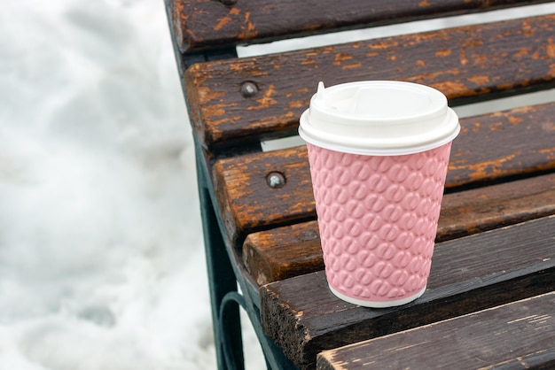 Una taza de café se encuentra en un banco de madera en el parque