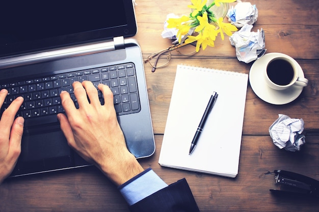 Una taza de café en un escritorio de madera con un hombre que trabaja en una computadora portátil