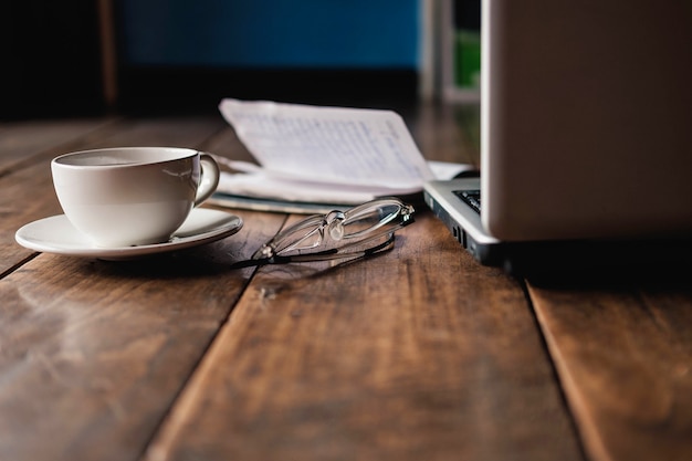 Una taza de café en el escritorio que tiene anteojos y una computadora portátil