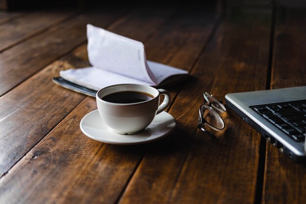 Una taza de café en el escritorio que tiene anteojos y una computadora portátil