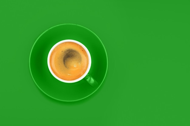 Una taza de café espresso completa con platillo sobre papel verde vivo, vista superior elevada, directamente encima