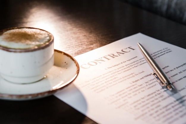 Taza de café con espuma y canela bolígrafo contrato en blanco sobre una mesa de madera