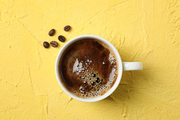 Taza de café con espuma espumosa y granos de café sobre fondo de color