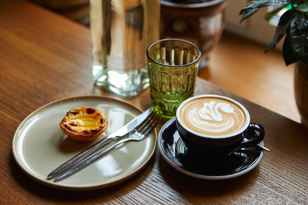 Taza de café con espuma y pastel en un plato con cubiertos