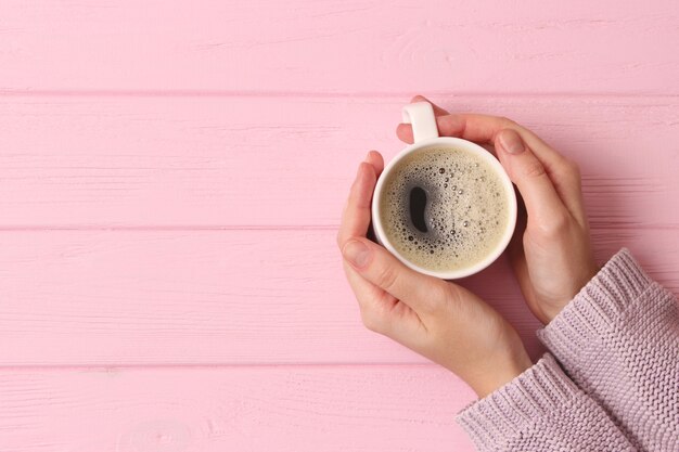 Taza de café con espumoso en manos femeninas en la vista superior de la mesa de madera